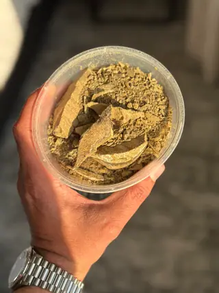 The tub of ambergris flakes from another angle, held in hand