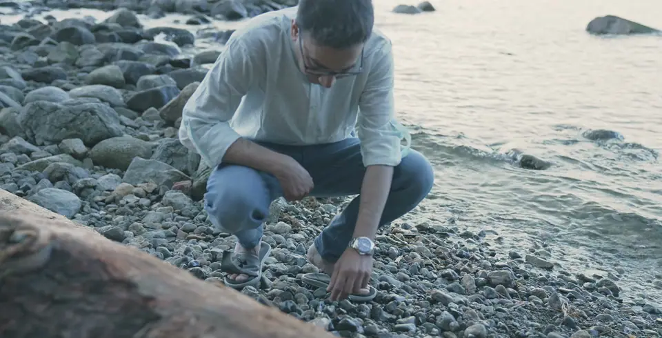 Nabil Valiulla crouching on a pebble beach to pick up a piece, from the founder film